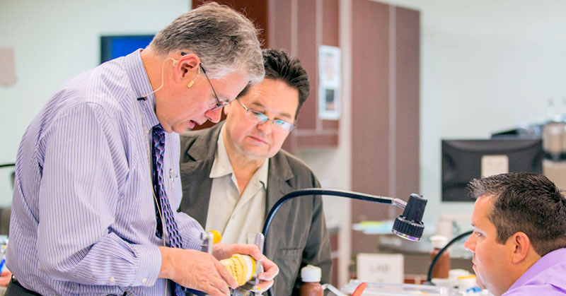 Dr. DeWood holding a set of molded teeth while a student watches.