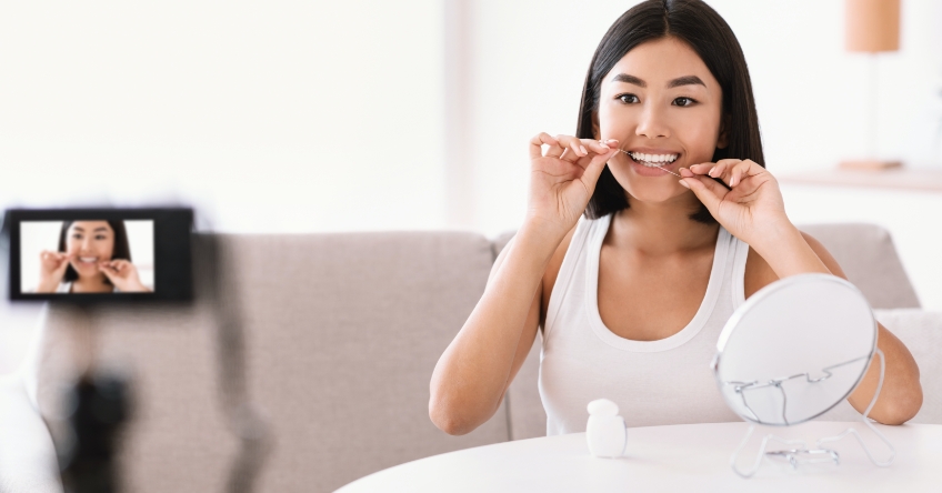 Woman recording herself flossing in front of tripod camera