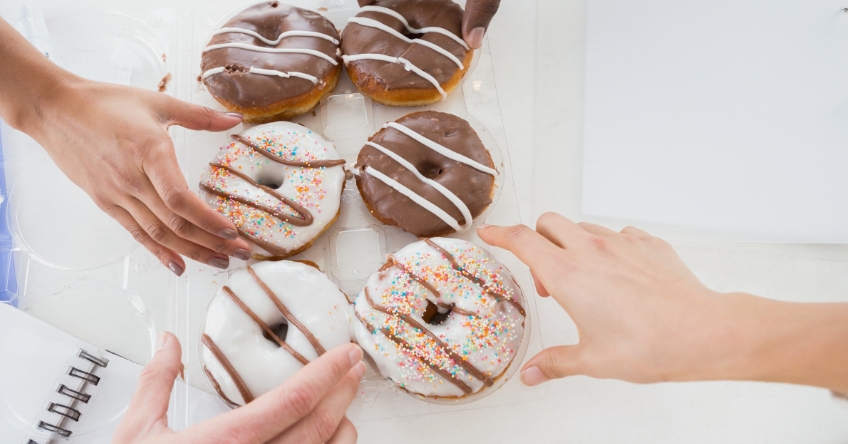 multiple hands grabbing donuts from office table